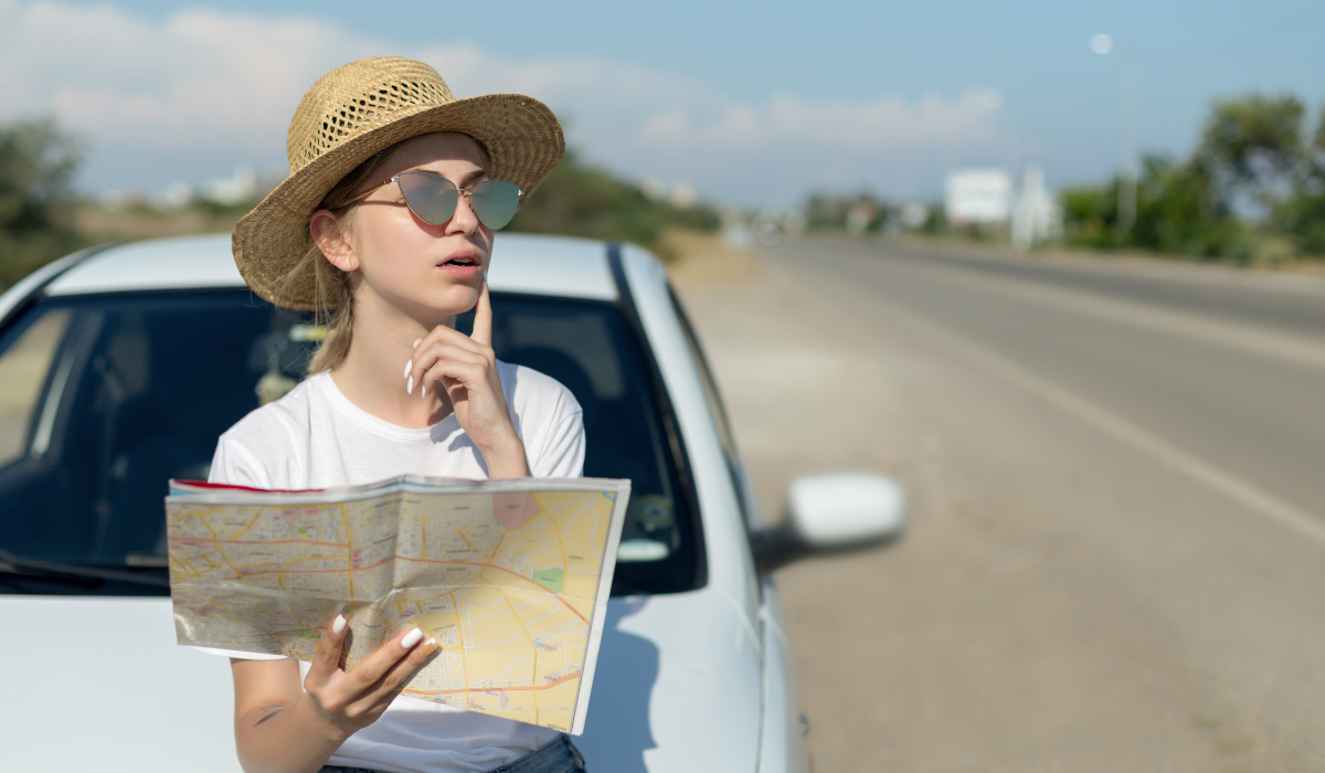 麦わら帽子とサングラスをかけ、地図を広げて道を確認する女性のポートレート